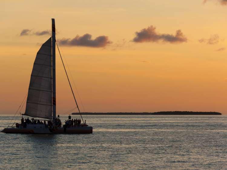 Catamaran sailing with tourists with a caribbean island behind at sunset.; Shutterstock ID 112369550; Invoice Number: -