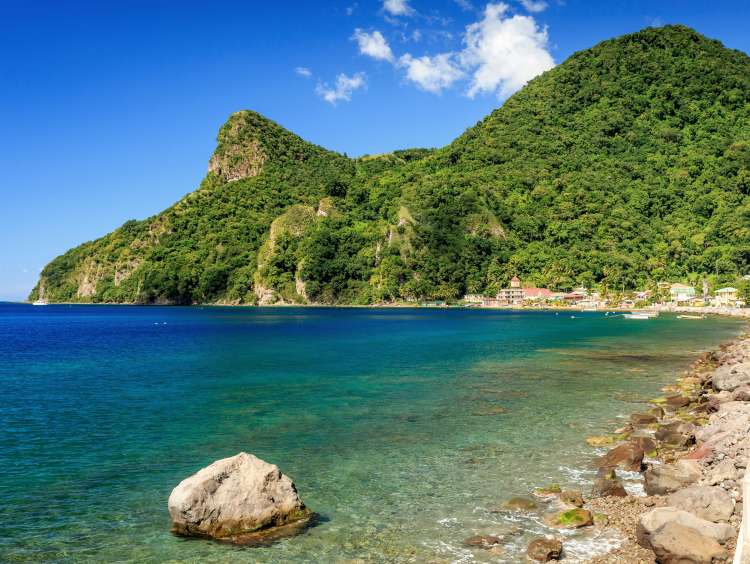 View across a bay with rocky shoreline, green hills and a terracotta-roofed village in the distance in Dominica, Caribbean