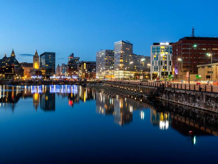 Brightly lit buildings line the waterfront at dusk in Liverpool, England, UK