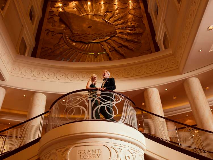 A couple stand at the top of the staircase in the Grand lobby on Queen Mary 2