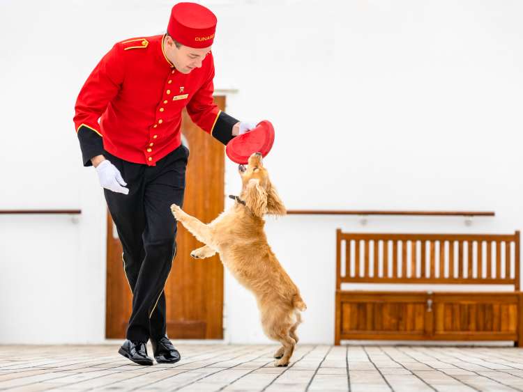 A Cunard bellboy plays with a dog on deck on Queen Mary 2