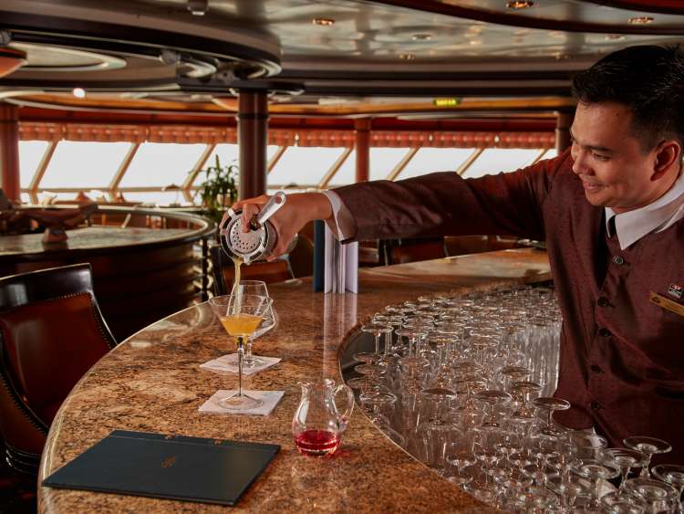 A barman pours a cocktail into a martini glass in the Commodore Club on board Cunard's Queen Victoria