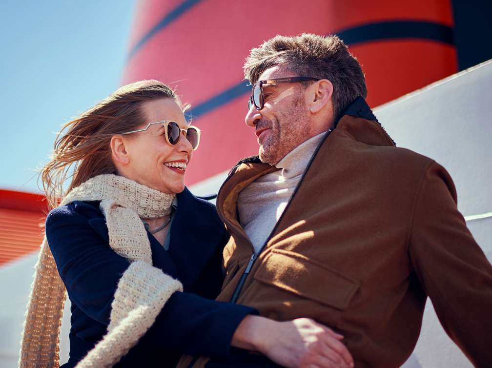 Couple relax on deck of a Cunard cruise ship in front of iconic red funnel