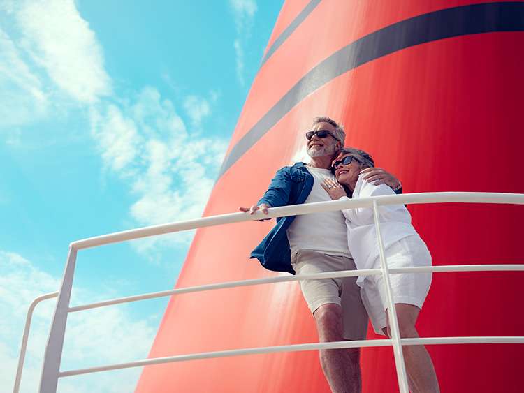 Couple enjoying the view on deck in front of the iconic red and black funnel of a Cunard cruise ship