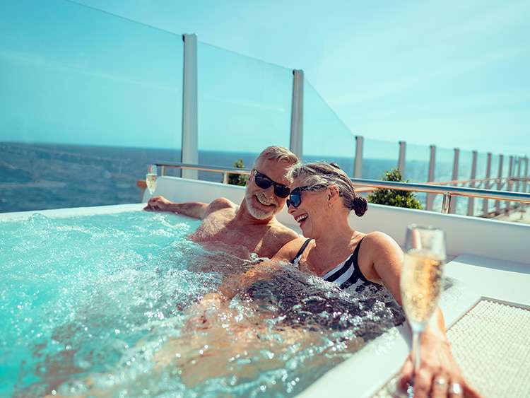 Couple enjoy glasses of champagne while sat in a jacuzzi on the Grills Terrace on board a Cunard cruise ship Queen Anne