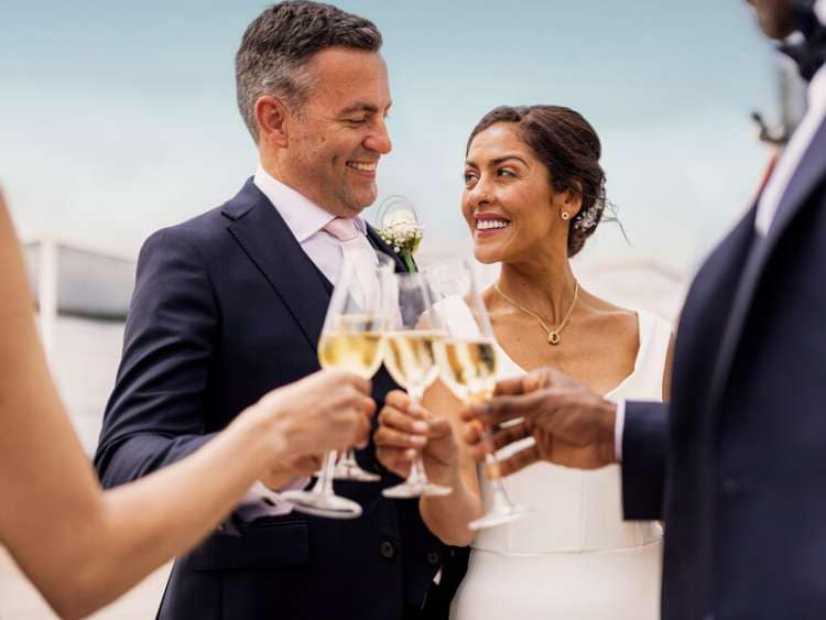 A bridge and groom clink glasses of champagne during a wedding on board a Cunard cruise ship