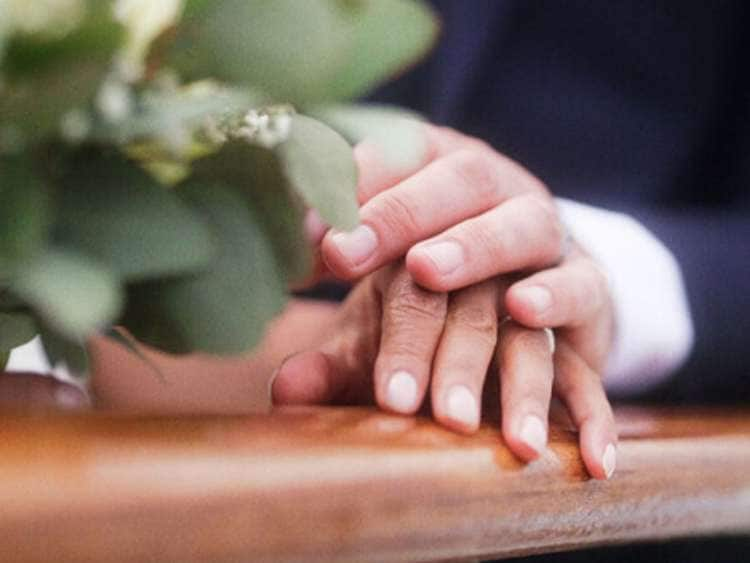 A bride and groom rest their hands on a railing of a Cunard cruise ship