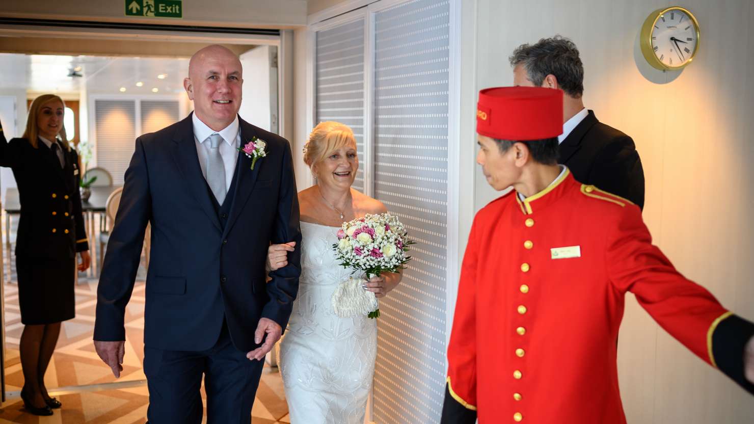 Cunard guests Debbie and Dale are escorted into the Admiral's Lounge by a Cunard bellhop for their wedding ceremony