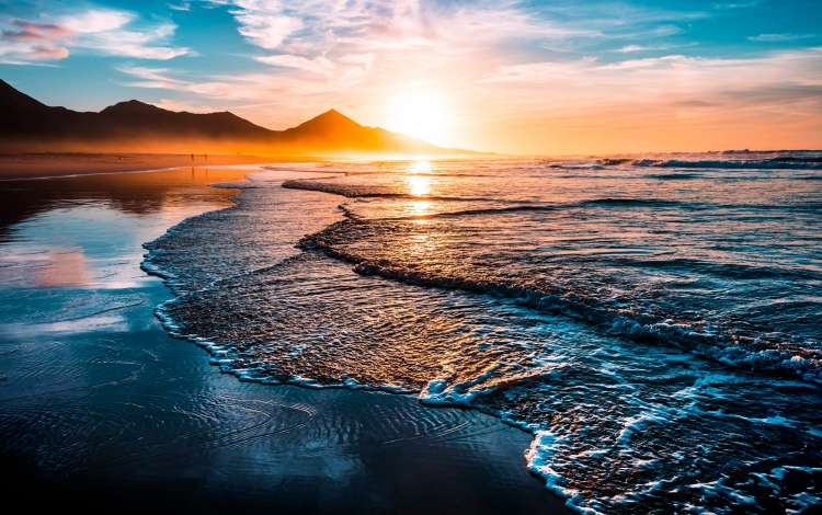 Amazing beach sunset with endless horizon and lonely figures in the distance, and incredible foamy waves. Volcanic hills in the background.; Shutterstock ID 746217742; purchase_order: n/a; job: Waves; client: cunard_digital; other: 