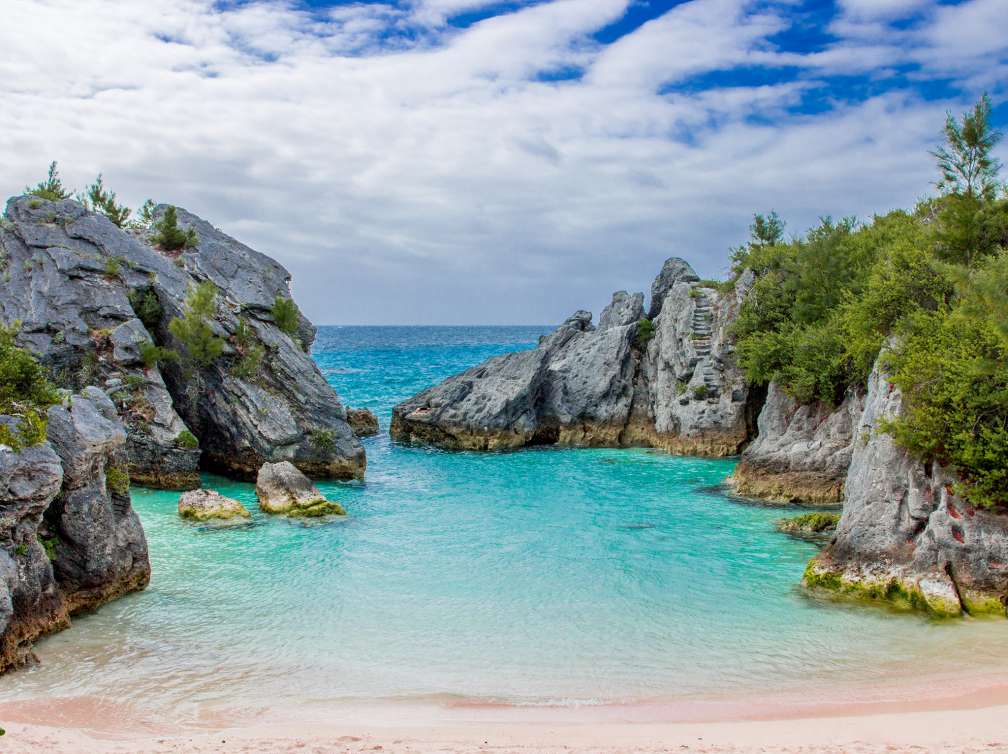 Bermuda coast with rocky cliffs either side meeting in the middle, small lagoon of water with grey skies in the background