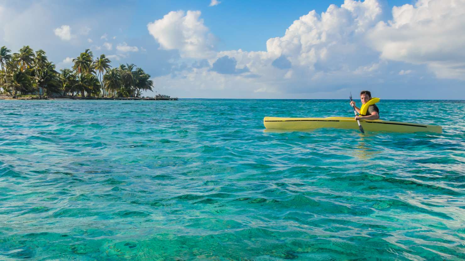 A man kayaks over clear Caribbean waters off the coast of Belize