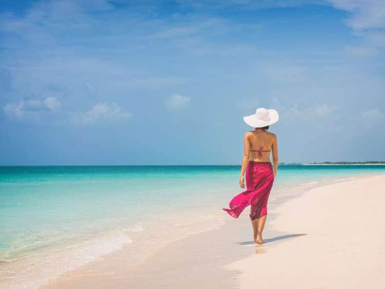 Luxury travel vacation elegant lady walking on beach in pink fashion skirt wrap relaxing on Caribbean holidays during winter.; Shutterstock ID 1398843719; purchase_order: n/a; job: Caribbean Guide; client: cunard_digital; other: 