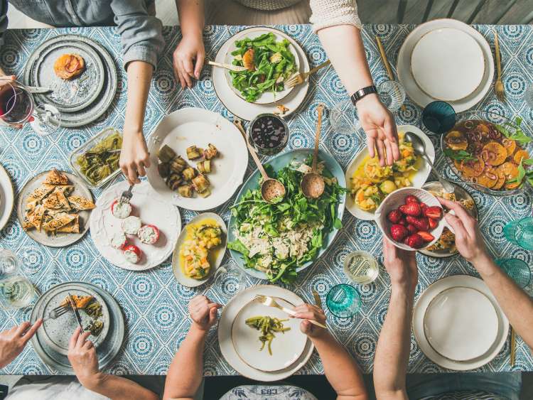 Mediterranean style dinner. Flat-lay of table with salads, starters, pastries over blue table cloth with hands holding drinks, sharing food, top view. Holiday gathering and vegetarian party concept; Shutterstock ID 1260599962; Purchase Order: -