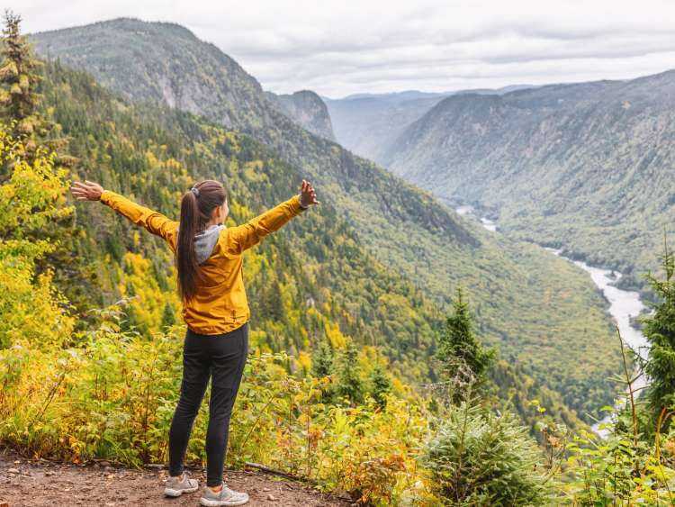 Happy woman hiking up mountain enjoying nature. Landscape with river view from top of trail hike. Girl with open arms outstretched in joy, enjoying travel fall in Jacques Cartier, Quebec, Canada. ; Shutterstock ID 1798308160; purchase_order: n/a; job: New England & Canada Guide; client: cunard-digital; other: As per agreed annual allowance