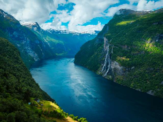 Lush forests and waterfalls border the blue water of Geirangerfjord in Norway