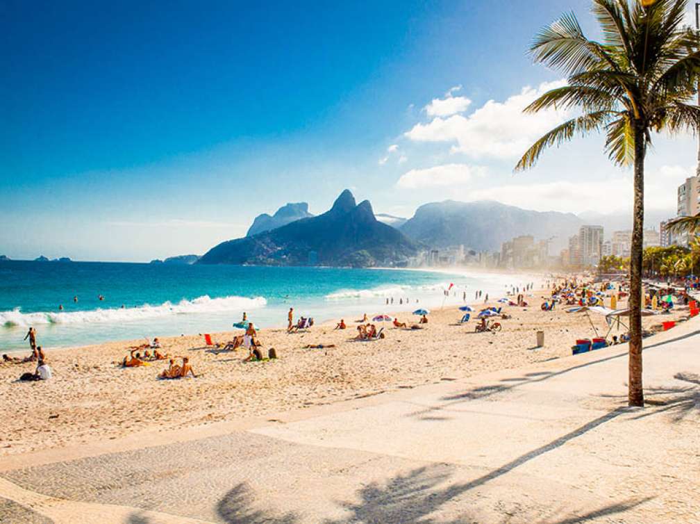 Beach in Brazil with mountains in the background and people playing in the sand and the ocean.