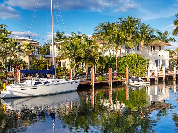 Fort Lauderdale sea front houses with a yacht docked, palm trees reflecting in the blue water 