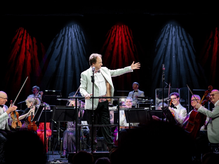 Anthony Inglis gestures thanks to the National Symphony Orchestra on the Royal Court Theatre stage on Queen Mary 2