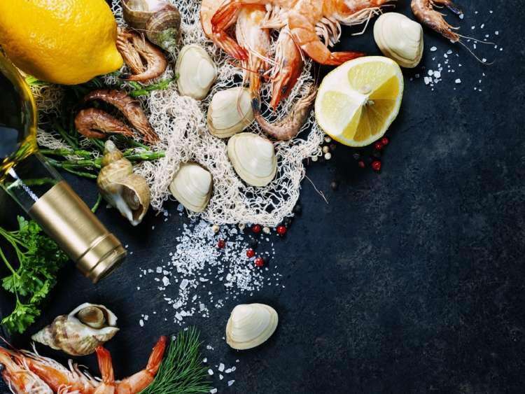 Delicious fresh fish and seafood on dark vintage background. Fish, clams and  shrimps with aromatic herbs, spices and vegetables - healthy food, diet or cooking concept