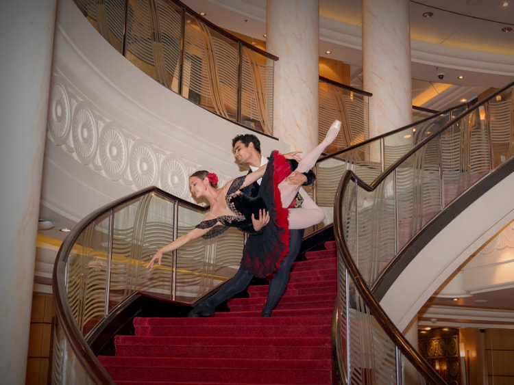 Two ballet dancers in costume pose on the grand atrium stairs on Cunard's Queen Mary 2