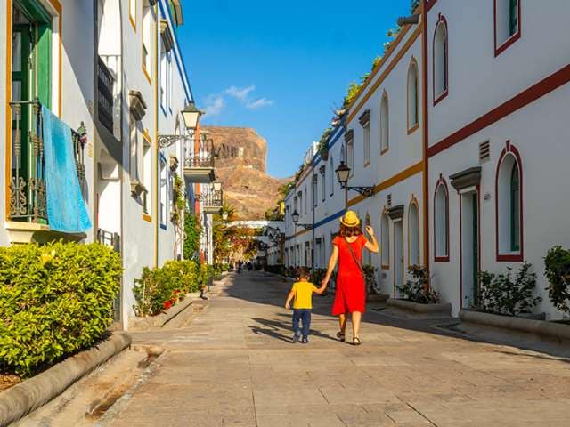 Mother in a red dress and her son walking in the port of the town Mogan in Gran Canaria