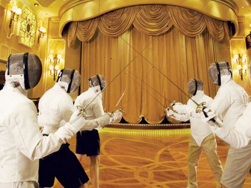 A group of guests in full fencing kit practicing their fencing moves in the Queens Room