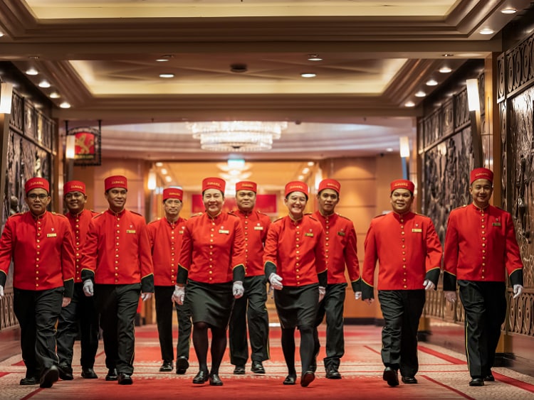 Ten bellhops in Cunard uniform walk through Queen Mary 2's elevator lobby