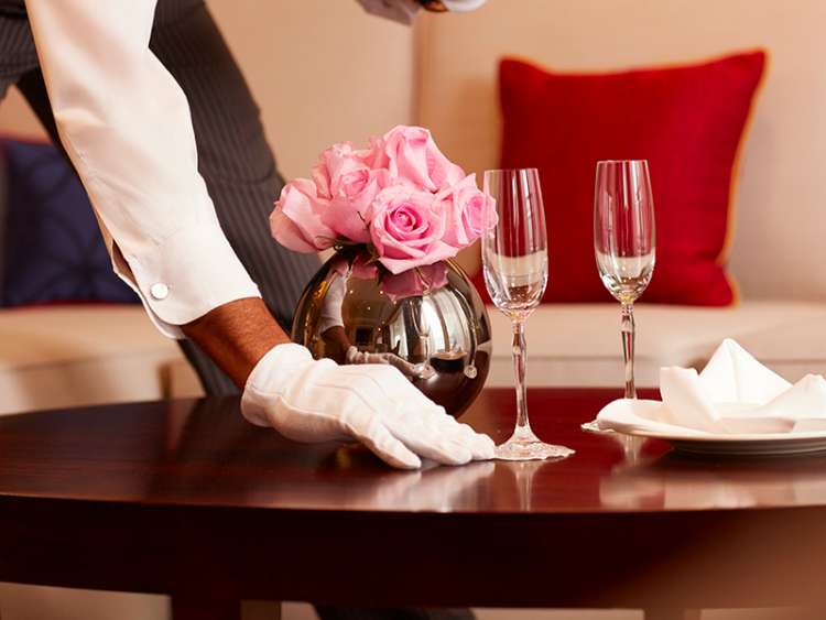 A butler placing champagne flutes on table in a stateroom on board a Cunard cruise ship