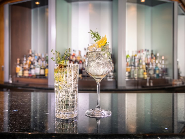 Two gin cocktails decorated with rosemary and lemon sit on a shining bar in Queen Mary 2's Verandah restaurant.