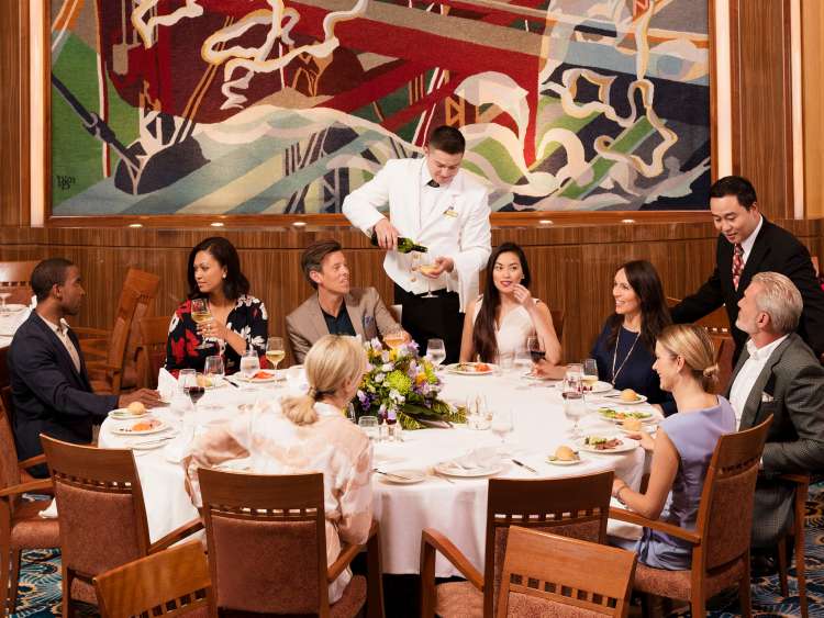 A group of guests dine at the Captain's table in Queen Mary 2's Britannia Restaurant