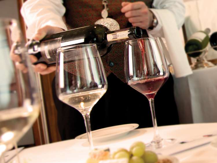 A sommelier pours red wine into a glass in one of our on board restaurants on Queen Mary 2