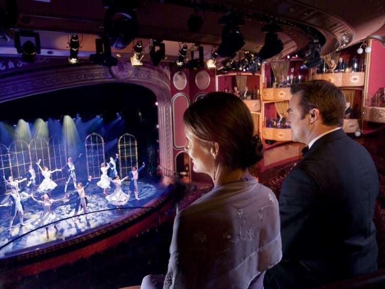 A man and a woman in evening dress watch a dance performance in the Royal Court Theater on board Cunard's Queen Victoria.