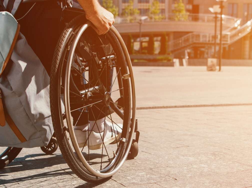 Man using wheelchair with bag on street with sunlight