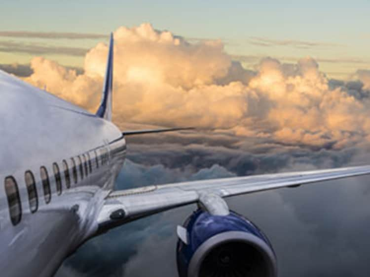 View alongside a passenger airplane flying through orange-lit clouds at sunset