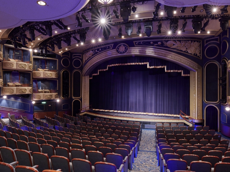 The Royal Court Theatre on Cunard's Queen Elizabeth, showing a curtained stage, rows of traditional theatre-style seating and boxes high up to the sides of the stage