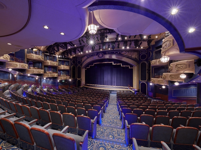 The Royal Court Theatre on Cunard's Queen Elizabeth, showing a curtained stage, rows of traditional theatre-style seating and boxes high up to the sides of the stage