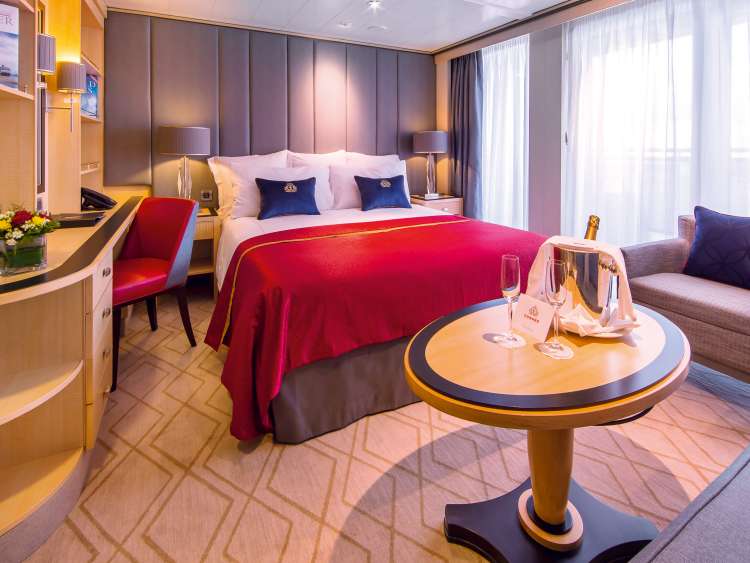 A remastered Princesss Grill suite on QM2, including double bed, desk, floor-to-ceiling windows and champagne ready to drink.