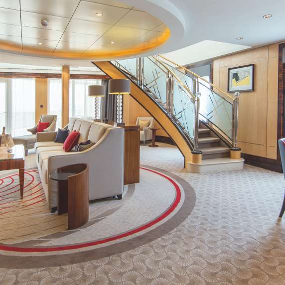 The lower level of the Balmoral Suite on Cunard's flagship, QM2.  A spacious lounge area, with dining table, balcony doors and sweeping staircase, are the centre to one of our most luxurious suites on board.