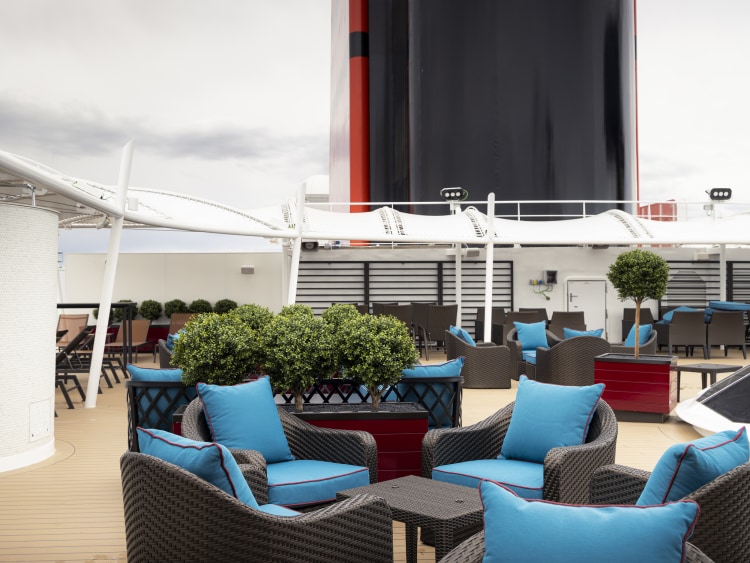 Queen Anne's Grills Terrace, exclusive deck area with outdoor seating, with red ship's funnel in background