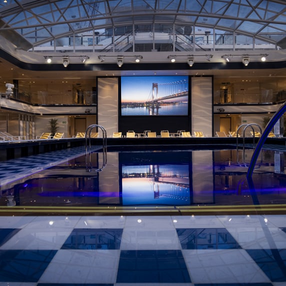 Nighttime view of Queen Anne's Pavilion venue, showing pool, dual-deck seating and cinema screen