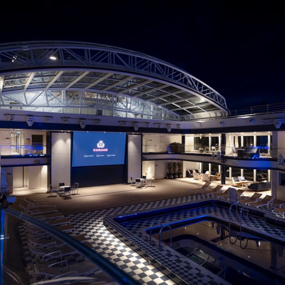 Nighttime view of Queen Anne's Pavilion venue, taken from the upper deck, showing pool, open roof and cinema screen