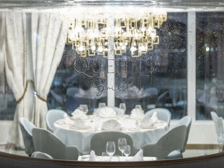 Tables set for dinner in Queen Anne's Queens Grill restaurant, shown through a glass screen