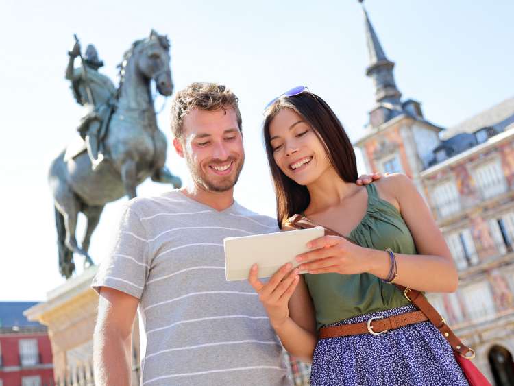 Madrid tourists using tablet travel app guidebook ebook on Plaza Mayor by statue of King Philip III. Tourist couple sightseeing visiting tourism landmarks and attractions in Spain. Young woman and man; Shutterstock ID 246070642; Purchase Order: -