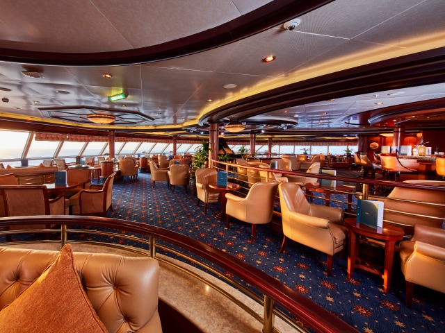 Wide shot of the Commodore Club on board Queen Victoria, showing bar, sea views and ample comfortable seating