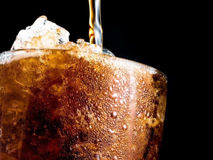 A soda being poured into a glass piled high with ice