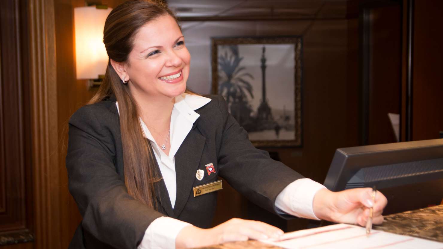 A smiling female Cunard crew member works at the on board reception desk 